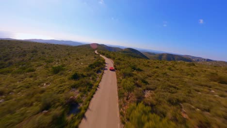 Vista-Aérea-De-Drones-Siguiendo-Un-Auto-Deportivo-Rojo-Conduciendo-A-Través-De-La-Pintoresca-Campiña-De-Cataluña,-España