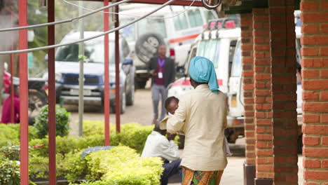 Toma-En-Cámara-Lenta-De-Una-Mujer-Mientras-Camina-Hacia-El-Marco-Sosteniendo-A-Un-Niño-Pequeño-En-Un-Hospital-Rural-En-Ruanda