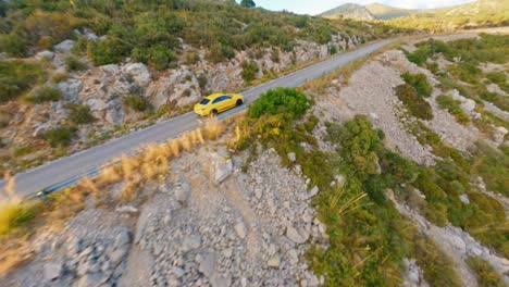 FPV-Drohne-Verfolgt-Einen-Gelben-Rennwagen,-Der-Auf-Einer-Bergstraße-In-Der-Malerischen-Spanischen-Landschaft-Rast