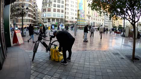 Glovo-Lieferfahrer-Verlässt-Das-Stadtrestaurant,-Um-Essen-Mit-Dem-Fahrrad-Zum-Kunden-Zu-Bringen-–-Valencia,-Spanien