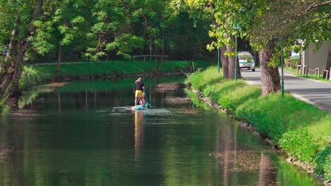 A-man-and-a-woman-on-stand-up-paddles-on-the-water-in-a-canal