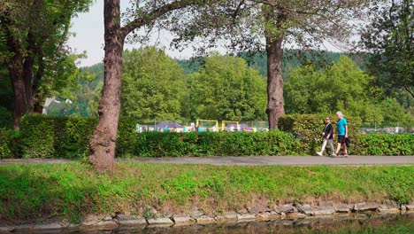 A-man-and-a-woman-walking-along-Lorettoweg-outside-the-lido-in-Klagenfurt,-Carinthia,-Austria