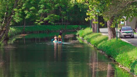 A-man-and-a-woman-on-stand-up-paddles-on-the-water-in-a-canal