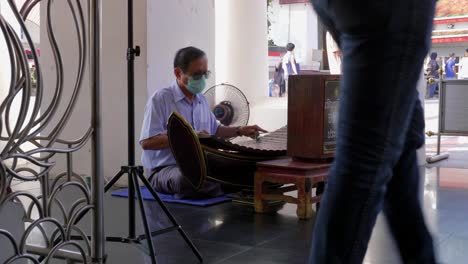 Asian-man-wearing-mask-playing-ranat-thai-xylophone-musical-instrument-in-buddhist-temple