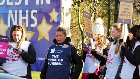 Overworked-NHS-workers-waving-banners-and-flags-in-fair-pay-strike-protest-on-picket-line-outside-hospital