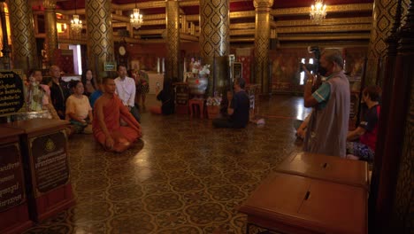 Fotógrafo-Tomando-Fotos-De-Monjes-Y-Turistas-Rezando-A-Buda-Dentro-Del-Templo-Budista,-Tailandia