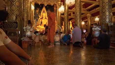 Monk-posing-for-pictures-with-Asian-family-near-Buddha-statue-in-Buddhist-temple,-Thailand