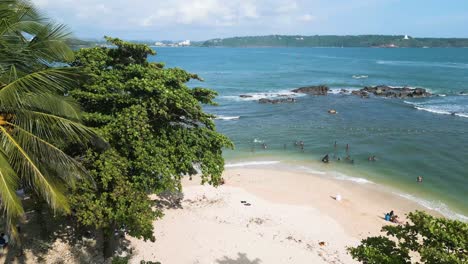 People-enjoy-the-beach,-aerial-shot,-coconut-trees,-and-waves-in-Sri-Lanka