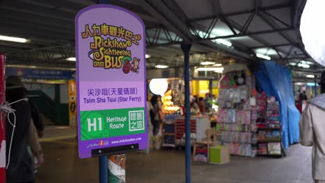 Schild-Am-Sightseeing-Busbahnhof-In-Hongkong-Und-Menschen,-Die-Dahinter-Laufen