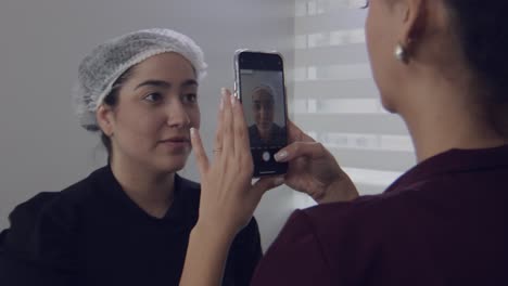 Paciente-De-Cirugía-Estética-Que-Recibe-Una-Fotografía-Con-Un-Smartphone-En-Una-Clínica-Por-Parte-De-Una-Enfermera,-Cámara-Lenta