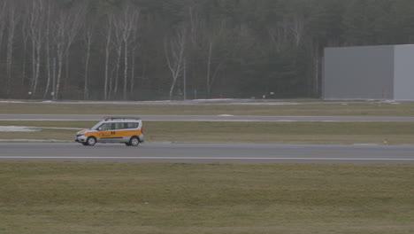 Toma-De-Seguimiento-Del-Automóvil-Del-Servicio-Del-Aeropuerto-Amarillo-Conduciendo-En-La-Pista-Del-Aeropuerto-De-Gdansk