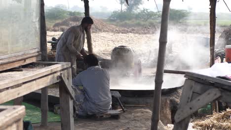 Cocineros-Masculinos-Vistos-En-Punjab-Rural-Junto-A-Una-Gran-Sartén-Y-Revolviendo-Con-Vapor-Saliendo-De-Ella,-Haciendo-Gur-Jaggery-A-Cámara-Lenta