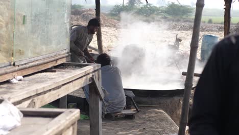 Cocineros-Masculinos-Vistos-En-Punjab-Rural-Al-Lado-De-Una-Gran-Sartén-Con-Vapor-Saliendo-De-Ella,-Haciendo-Gur-Jaggery-A-Cámara-Lenta