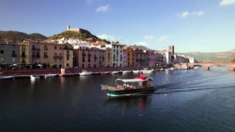 Seguimiento-Aéreo-Del-Crucero-Turístico-En-Barco-Por-El-Canal-Con-Una-Ciudad-Medieval-De-Color-En-El-Fondo