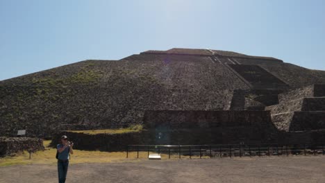 A-slow-motion-panning-shot-of-the-Pyramid-of-the-Sun-in-the-archaeological-zone-of-Teotihuacan,-Mexico,-with-tourists-watching-and-taking-pictures-on-a-clear-and-sunny-day