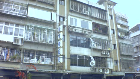 Taipei,-Taiwan---Jan-28th-2019:-horizontal-view-of-ghetto-old-dirty-asian-apartment-building-with-advertisement-billboard-signs-of-Chinese-clinic-and-Lily-dry-wash-and-all-bared-window-balcony