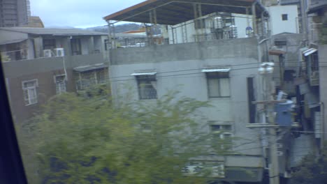 Taipei,-Taiwan---Jan-28th-2019:-riding-in-sky-metro-train-railroad-view-of-ghetto-slum-city-urban-town-with-old-rusty-concrete-building-and-metal-bars-on-windows-and-traffic-road-with-cars-and-scooter