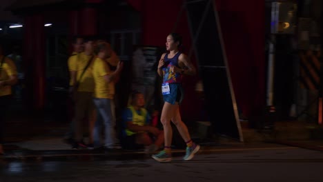 female-athlete-running-and-taking-a-water-break-during-the-Samui-Run,-Koh-Samui-Island,-Thailand