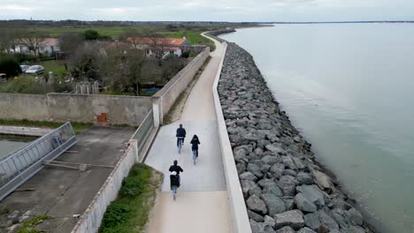 Menschen,-Die-Mit-Dem-Fahrrad-An-Der-Dorfpromenade-Am-Meer-Entlang-Fahren,-Luftaufnahme