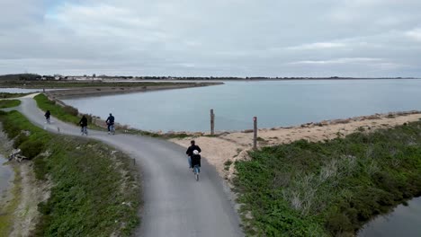 Familie-Fährt-Fahrrad-In-Ufernähe,-Kleinkind-Fährt-Auf-Dem-Fahrrad-Des-Vaters,-Luftaufnahme-Von-Hinten