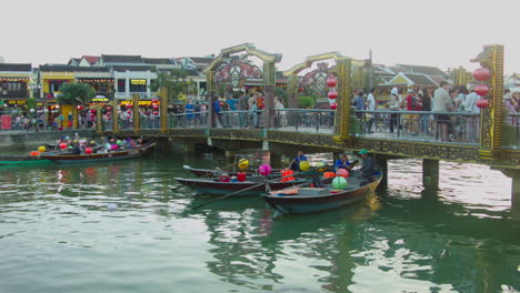 Vista-Cinematográfica-Del-Puente-Peatonal-Sobre-El-Río-Con-Botes-Flotando-En-El-Río-Al-Atardecer-En-El-Casco-Antiguo-De-Hoi-An,-Vietnam