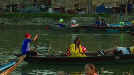 Mujer-Turista-Haciendo-Clic-En-Selfies-Mientras-Viaja-En-Un-Barco-Tradicional-De-Madera-En-La-Antigua-Ciudad-De-Hoi-An-Con-Otros-Barcos-Y-Turistas-En-El-Fondo,-Vietnam