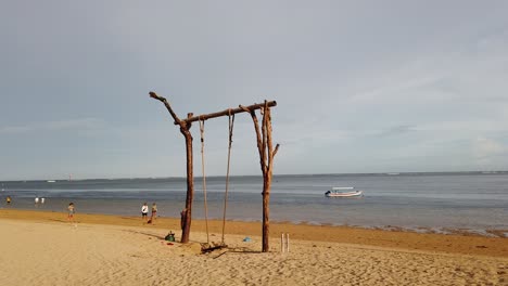 Balinese-Hammock-on-Sanur-beach-Tourists-Walking-By-the-Sea-Coast-of-White-Sand-Popular-Asian-Destination,-Bali-Indonesia