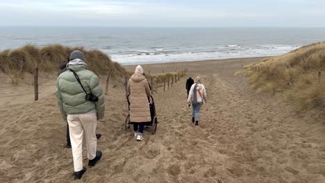 Grupo-Familiar-Caminando-Cuesta-Abajo-Por-Las-Dunas-De-Arena-Hacia-El-Mar-Del-Norte-En-Países-Bajos---Imágenes-En-Cámara-Lenta