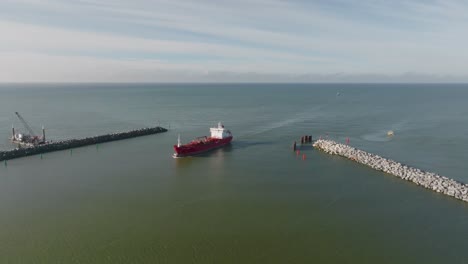 Aerial-view:-a-red-cargo-ship-sails-through-the-port-gates-of-Klaipeda-city