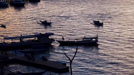 Siluetas-De-Personas-Durante-La-Oscura-Luz-Del-Atardecer-Trabajando-En-La-Descarga-De-Pequeños-Botes-En-El-Puerto-De-Labuan-Bajo-En-La-Isla-De-Flores,-Indonesia