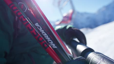 Close-up-of-the-ski-poles-of-a-person-being-towed-on-the-ski-lift-to-ski-the-top-of-a-snowy-mountain