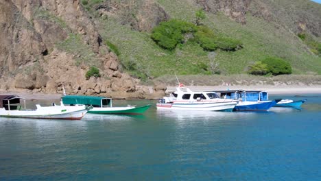 Barcos-Amarrados-En-Una-Playa-Aislada-De-Arena-Blanca-Con-Aguas-Turquesas-Y-Montañas-Escarpadas-En-La-Isla-Tropical-De-Padar-En-El-Parque-Nacional-De-Komodo,-Este-De-Nusa-Tenggara,-Indonesia