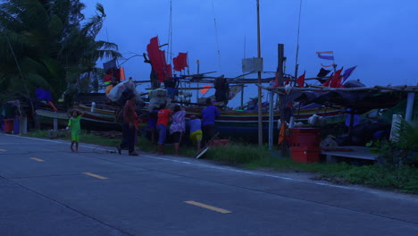 Grupo-De-Personas-Empujando-Un-Bote-Tradicional-Tailandés-De-Madera-En-La-Orilla-Con-Fuertes-Vientos,-Songkhla,-Tailandia