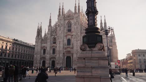 Frontal-view-of-Duomo-Milano-Cathedral-in-Milan-with-people-walking-on-open-square,-camera-movement,-downtown-view-of-Italian-city-with-tourists