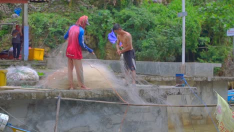 Two-Fishermen-at-harbor-pulling-fishing-net-out-of-boat-after-catch,-static-medium-shot