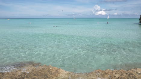 Menschen-Schwimmen,-Tauchen-Und-Baden-Im-Blauen-Meer-Mit-Katamaran-Im-Hintergrund