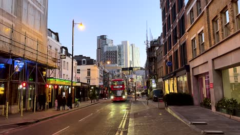 Red-London-bus-driving-through-streets-of-Shoreditch-with-skyscrapers