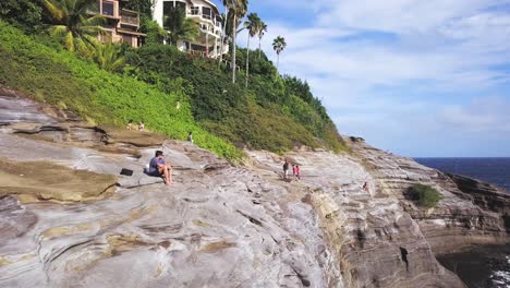 Ein-Abenteurer-In-Der-Spitting-Cave-In-Honolulu,-Hawaii,-Sitzt-Auf-Einer-Klippe-Und-Genießt-Die-Landschaft-–-Lufttransportschwenk