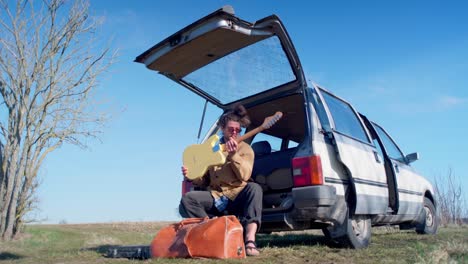 Attraktiver-Mann,-Der-Gitarre-Spielt,-Während-Er-Auf-Dem-Rücksitz-Eines-Autos-In-Der-Sonne-Sitzt