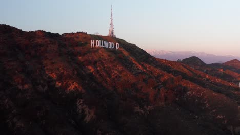 Toma-Panorámica-Aérea-De-Primer-Plano-Del-Cartel-De-Hollywood-Al-Atardecer-Con-Montañas-Cubiertas-De-Nieve-En-El-Fondo