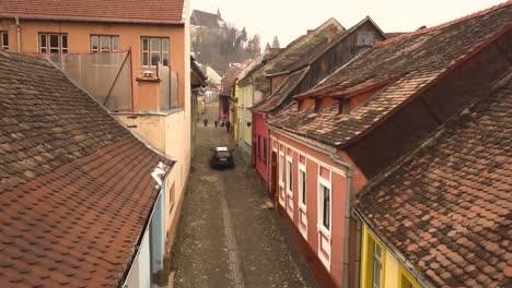 Auto-Fährt-An-Der-Steinstraße-Der-Berühmten-Mittelalterlichen-Stadt-Sighisoara-Vorbei,-Mit-Der-Kirche-Auf-Der-Spitze-Des-Hügels-Im-Hintergrund