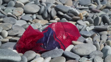 Rote-Plastiktüte-Verstreut-Einen-Kiesstrand,-Der-Von-Links-Nach-Rechts-Schwenkt