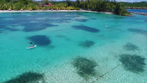 Slow-motion-aereal-view-of-people-paddleboarding-near-a-resort’s-beach-on-the-Honduran-caribbean-sea