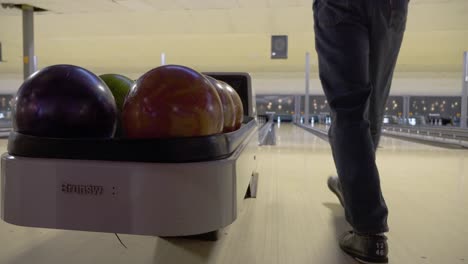 A-low-angle-shot-of-a-man-grabbing-a-bowling-ball-and-going-to-throw-it-at-the-top-of-the-aisle-in-a-bowling-alley