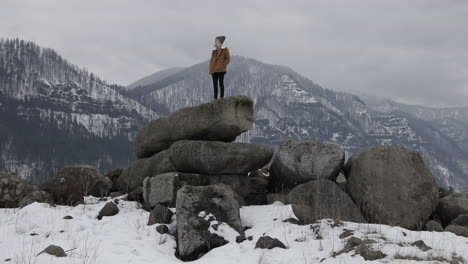 A-girl-stands-on-boulders-with-snowy-mountains-around-her