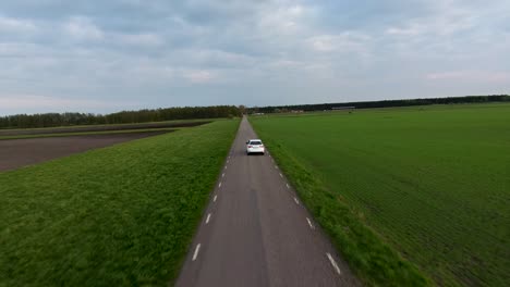 Große-Luftdrohnenaufnahme-Eines-Weißen-Autos,-Das-Auf-Der-Schmalen-Landstraße-In-Südschweden-Skåne-Fährt