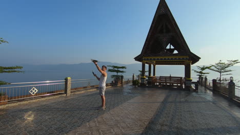 Man-hand-launching-drone-and-flying-it-into-the-distance-on-a-rooftop-patio-overlooking-a-lake-in-Indonesia