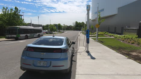 Editorial,-Vista-De-La-Carga-Del-Coche-Eléctrico-Afuera-En-La-Calle-Al-Lado-Del-Paseo-Y-Un-Autobús-Al-Otro-Lado-De-La-Calle