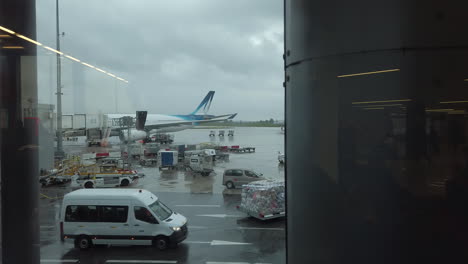 Camión-Dolly-Izquierdo-En-Aviones-Y-Vehículos-En-El-Trabajo-En-La-Pista-Asfaltada-En-El-Aeropuerto-De-París-Orly-Antes-Del-Despegue,-Vista-Desde-La-Zona-De-Embarque