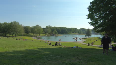 Editorial,-beautiful-view-of-nature-park,-lake-,-summer-moment,-beautiful-weather,-blue-sky,-people-sitting-on-grass-beside-and-in-front-of-the-lake,-smooth-zoom-in